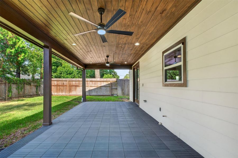 Spacious covered patio with elegant wood ceiling and modern fans, overlooking a lush, private fenced backyard.