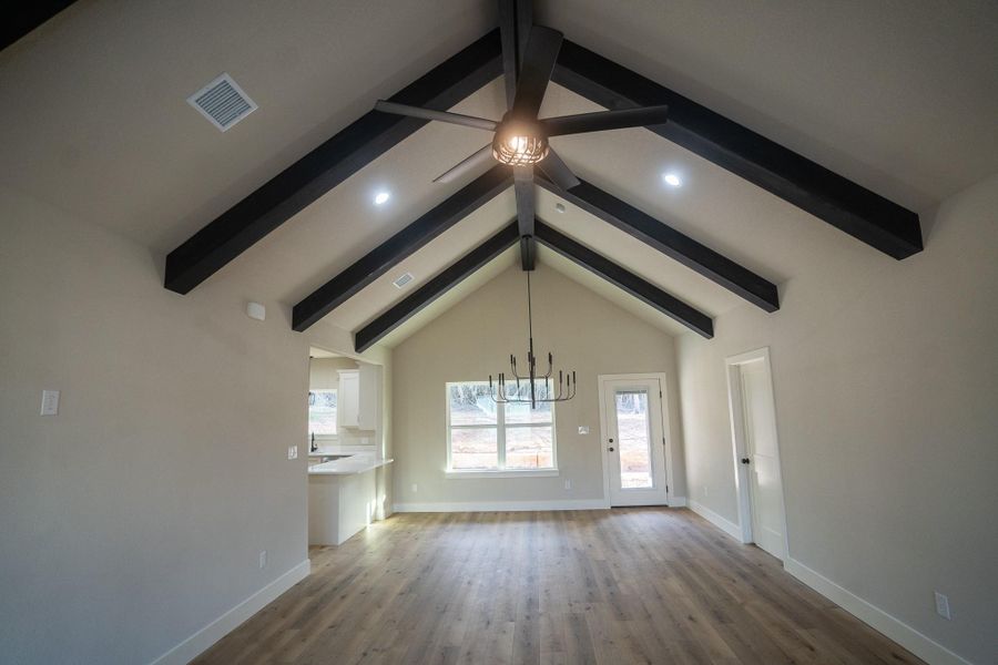 Unfurnished living room with wood finished floors, visible vents, baseboards, vaulted ceiling with beams, and ceiling fan