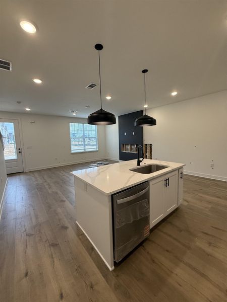 Kitchen with open floor plan, white cabinets, dishwasher, hanging light fixtures, and an island with sink