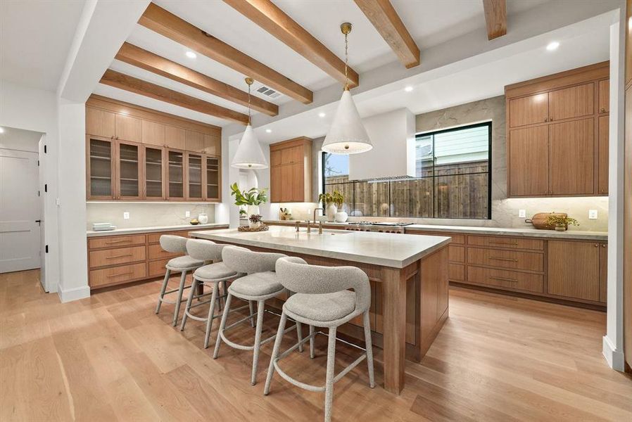 Kitchen with a breakfast bar, beam ceiling, tasteful backsplash, pendant lighting, and a center island with sink Kitchen with a breakfast bar, beam ceiling, tasteful backsplash, pendant lighting, and a center island with sink