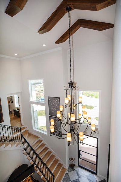 This photo showcases a bright entryway with high ceilings and a grand chandelier. The space features a modern staircase with elegant iron railings, large windows for natural light, and a stylish tiled floor.