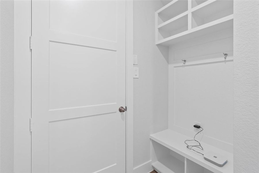 Step into this highly functional and stylish mudroom drop zone, an essential feature for a busy household. The space boasts custom-built white cabinetry and shelving, providing generous storage for coats, bags, and shoes. A comfortable built-in bench offers a convenient spot to sit, while three sleek hooks keep outerwear tidy and accessible.