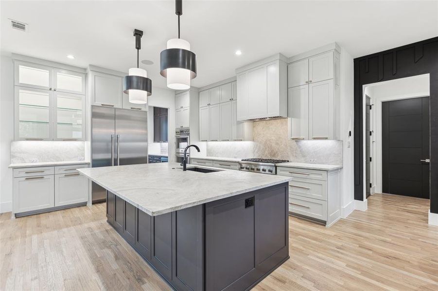 Kitchen with hanging light fixtures, decorative backsplash, an island with sink, sink, and light hardwood / wood-style floors