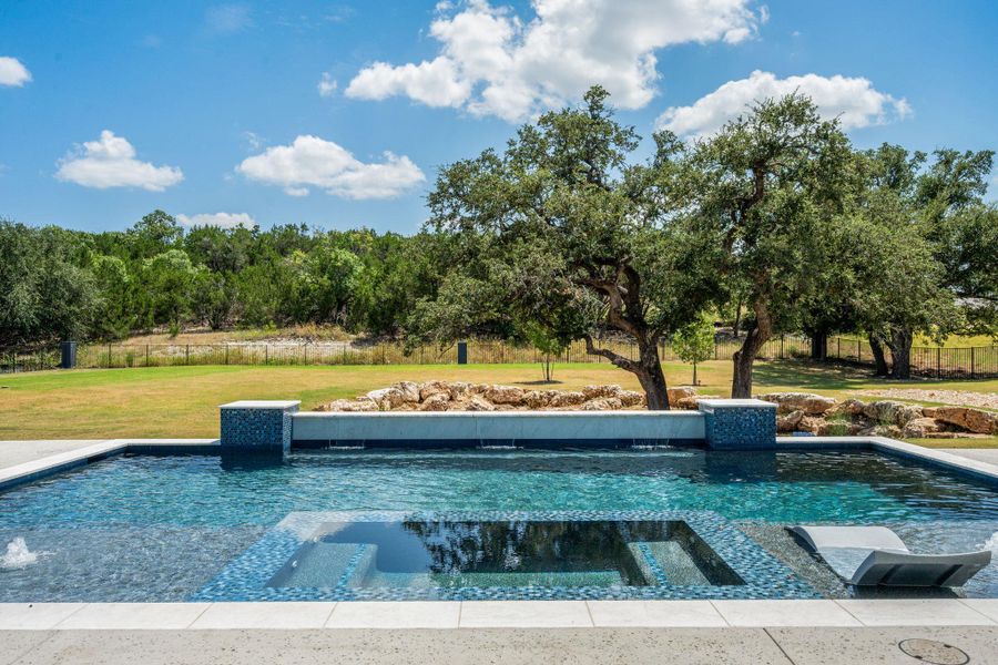 A sparkling swimming pool looks out over mature trees and a manicured lawn.