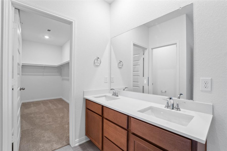 This beautifully updated primary bathroom is move-in ready! It showcases stained cabinetry paired with light countertops, dual vanity sinks, a large mirror, a spacious walk-in closet with built-in shelving, high ceilings, custom paint, and stylish modern finishes throughout.