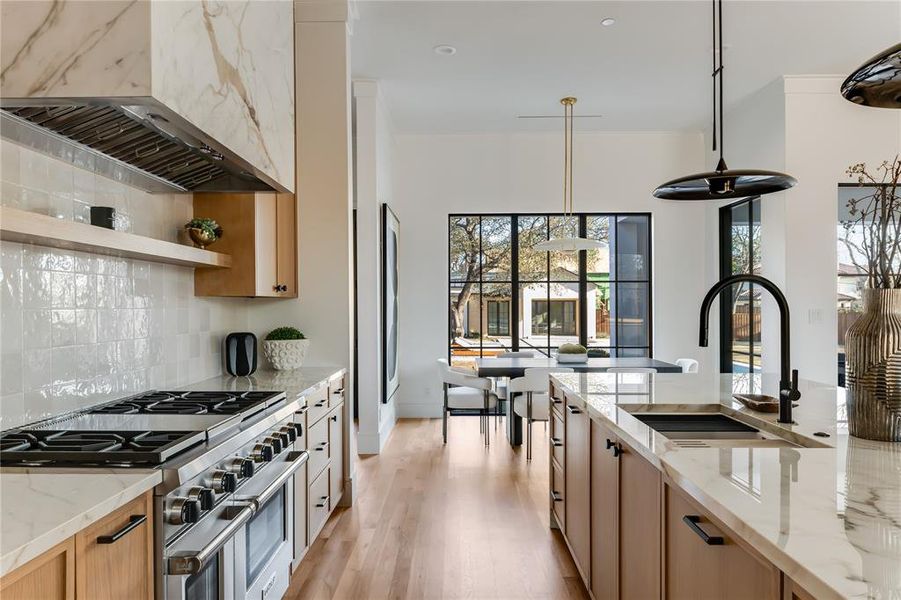 Kitchen with sink, wall chimney range hood, double oven range, hanging light fixtures, and light stone countertops