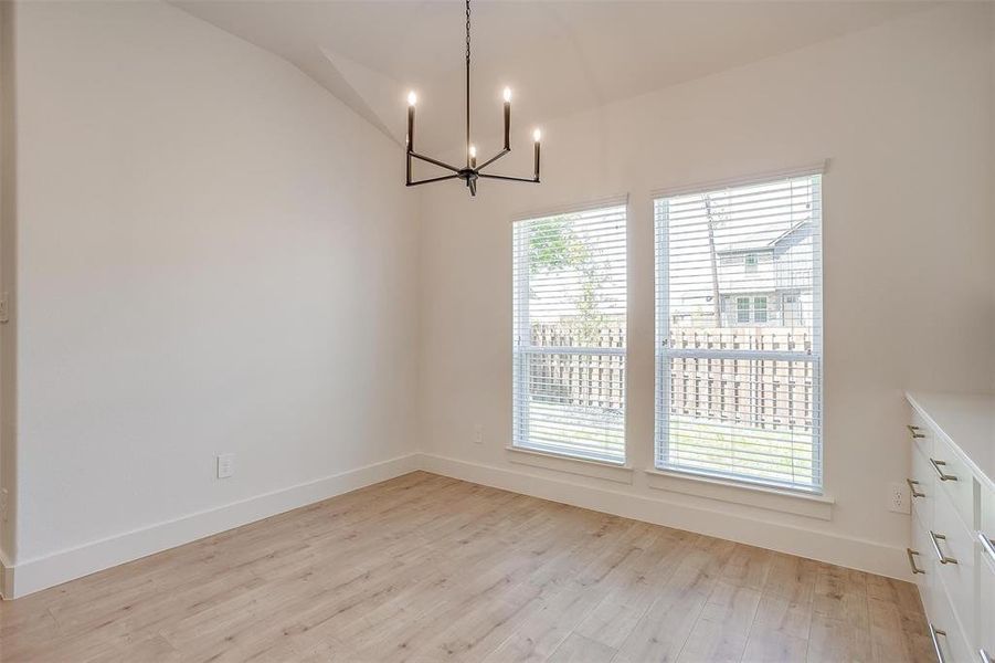 Unfurnished dining area with a wealth of natural light, an inviting chandelier, light hardwood / wood-style flooring, and lofted ceiling