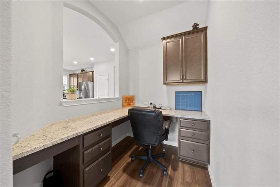 Office area with luxury vinyl flooring, built in desk, storage and lofted ceiling.