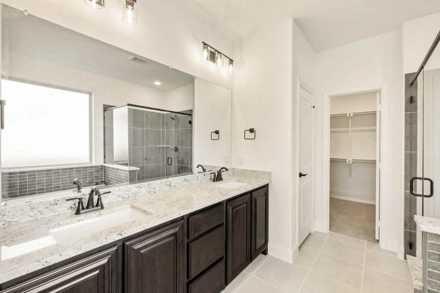 Master bathroom with double vanity, granite countertops, glass shower, and walk-in closet entrance