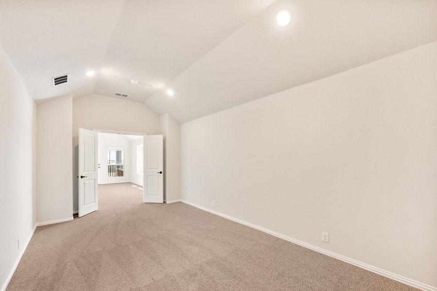 Empty bedroom with vaulted ceiling, beige carpet, and open double doors leading to hallway Empty bedroom with vaulted ceiling, beige carpet, and open double doors leading to hallway