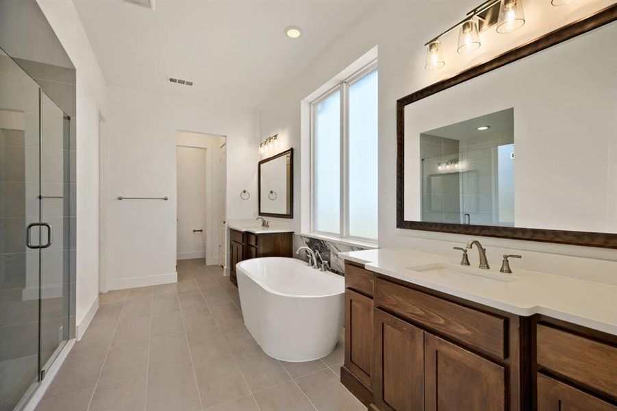 Bathroom with two vanities, a freestanding bath, a shower stall, light tile patterned floors, and recessed lighting