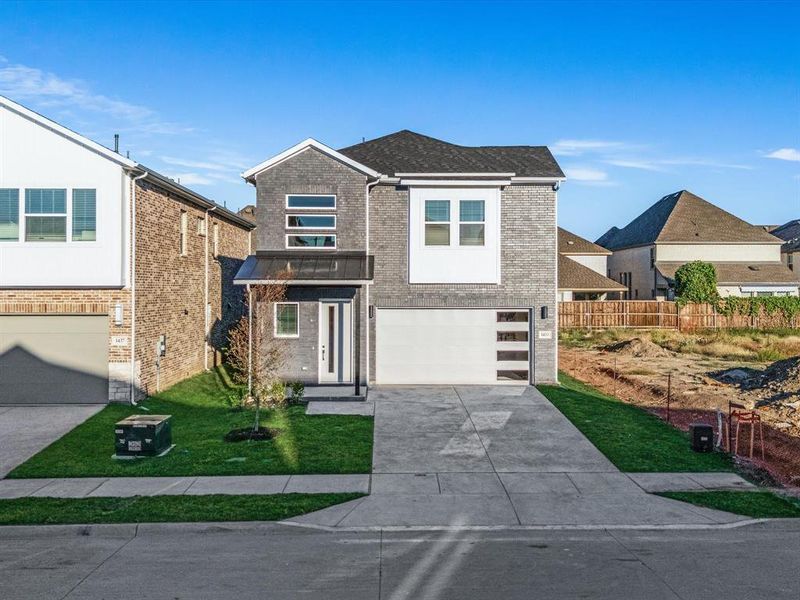 Contemporary house featuring brick siding, driveway, a front yard, an attached garage, and roof with shingles