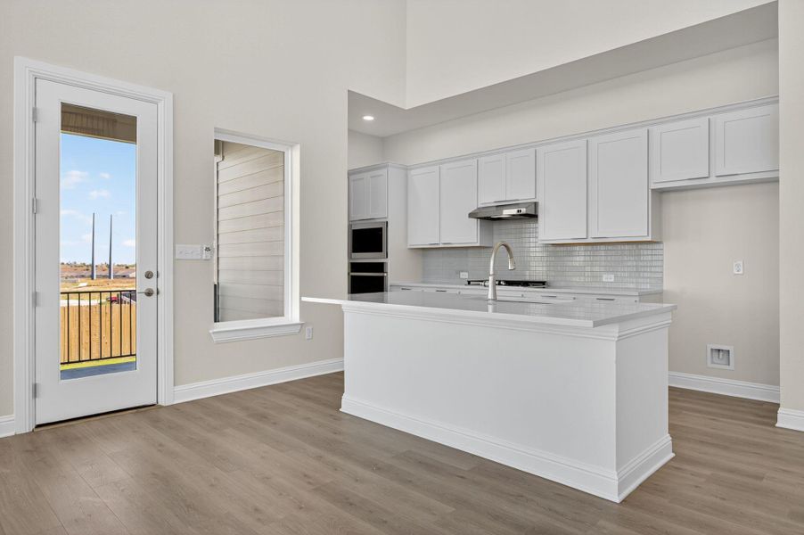Kitchen featuring white cabinets, light wood-style floors, a kitchen island with sink, light stone counters, and tasteful backsplash