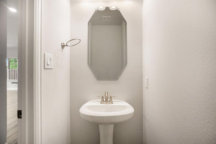 This photo shows a modern half bathroom with a pedestal sink, a stylish mirror, and neutral walls.