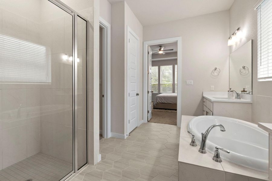 Bathroom featuring a built-in soaking tub with deck-mounted fixtures, a glass-enclosed shower, a white vanity with an integrated sink, and hexagon tile flooring