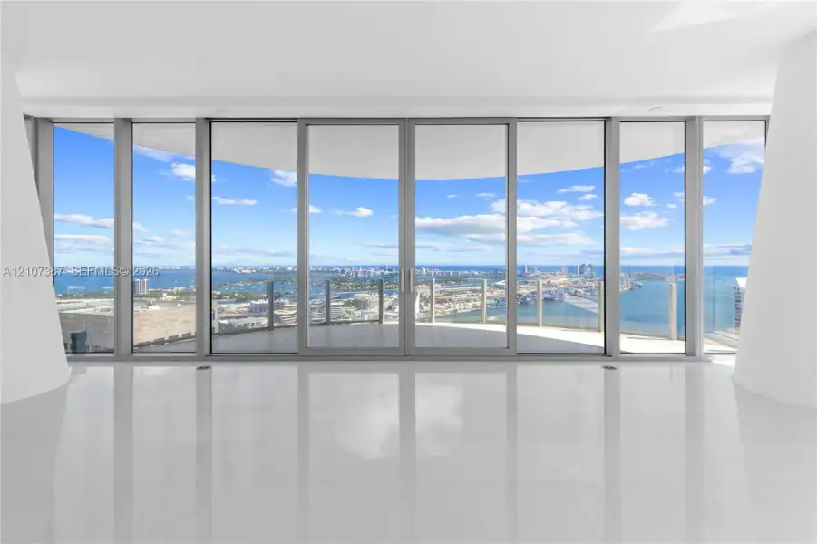 Floor-to-ceiling glass walls, expansive curved balcony with a glass railing, polished tile flooring, and structural white pillars