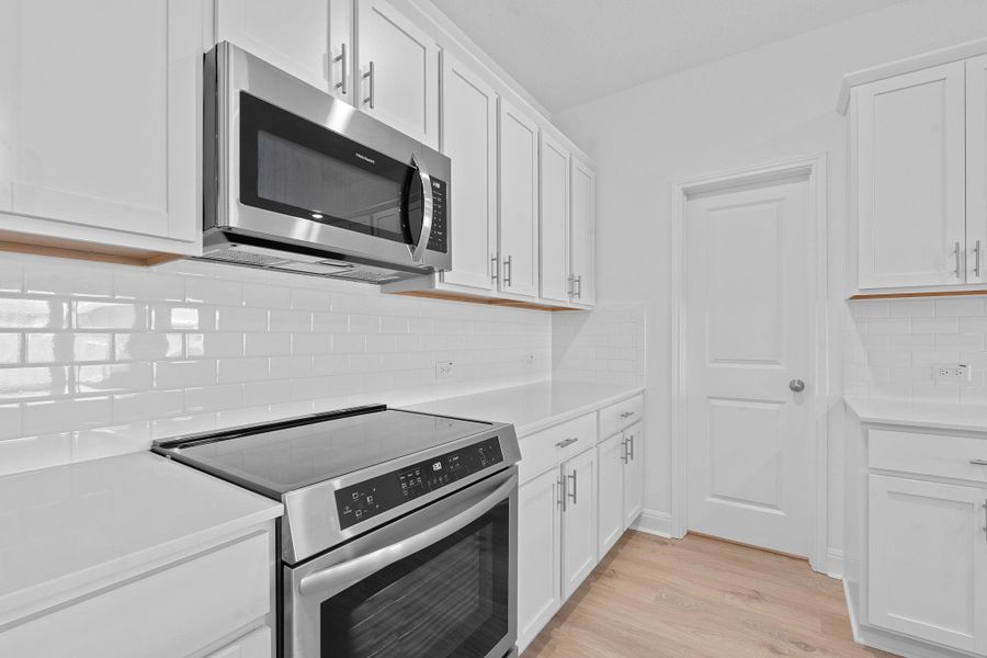 Kitchen featuring stainless steel appliances, white cabinetry, backsplash, and light wood-style floors Kitchen featuring stainless steel appliances, white cabinetry, backsplash, and light wood-style floors