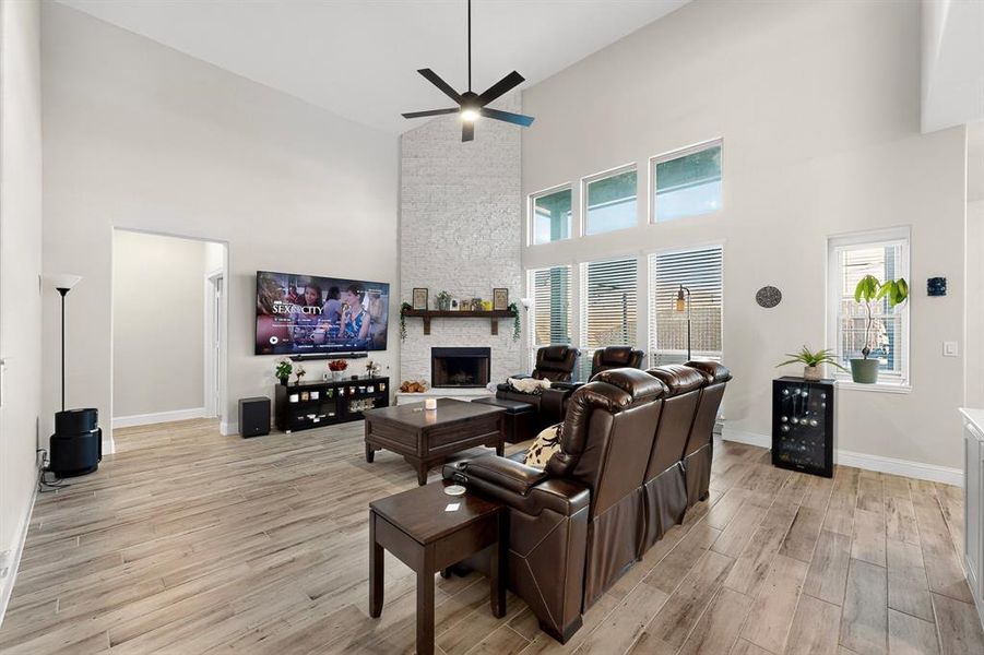 Living room with a towering ceiling, a fireplace, light wood-type flooring, a ceiling fan, and beverage cooler Living room with a towering ceiling, a fireplace, light wood-type flooring, a ceiling fan, and beverage cooler