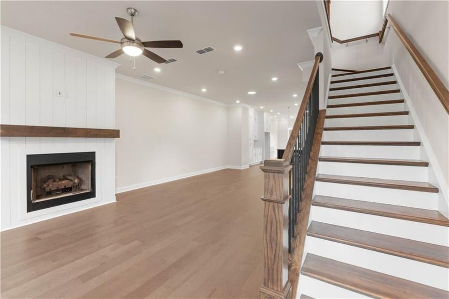 Stairs featuring wood finished floors, a fireplace, recessed lighting, crown molding, and ceiling fan