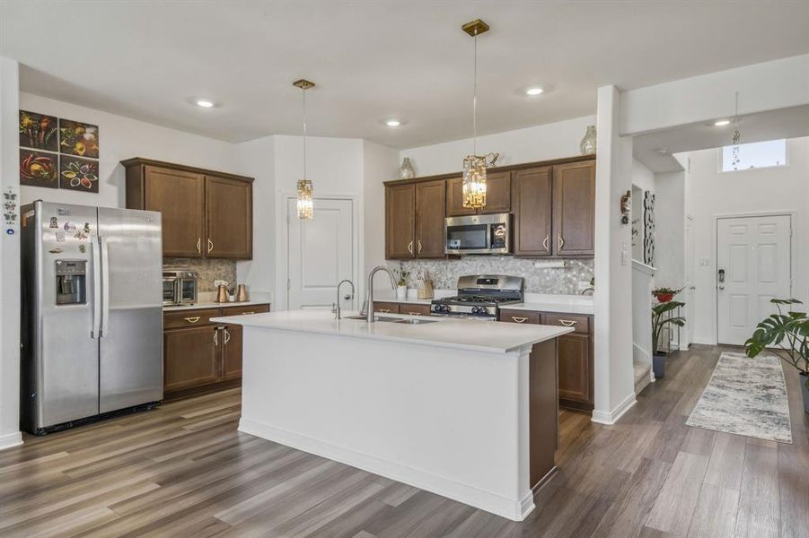 Contemporary kitchen featuring wood-finish flooring, a central island with a solid surface countertop, stainless steel appliances, and dark wood cabinetry Contemporary kitchen featuring wood-finish flooring, a central island with a solid surface countertop, stainless steel appliances, and dark wood cabinetry