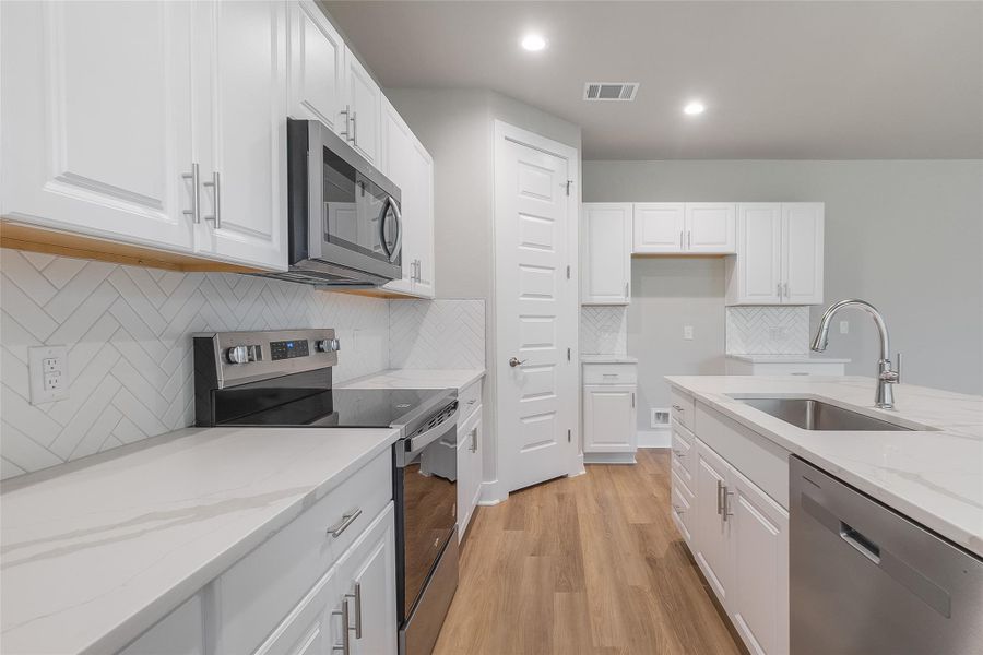 Modern white kitchen with natural lighting, quartz countertops, sleek cabinetry, stainless appliances, recessed lighting, large center island, pantry, and modern backsplash design. Modern white kitchen with natural lighting, quartz countertops, sleek cabinetry, stainless appliances, recessed lighting, large center island, pantry, and modern backsplash design.