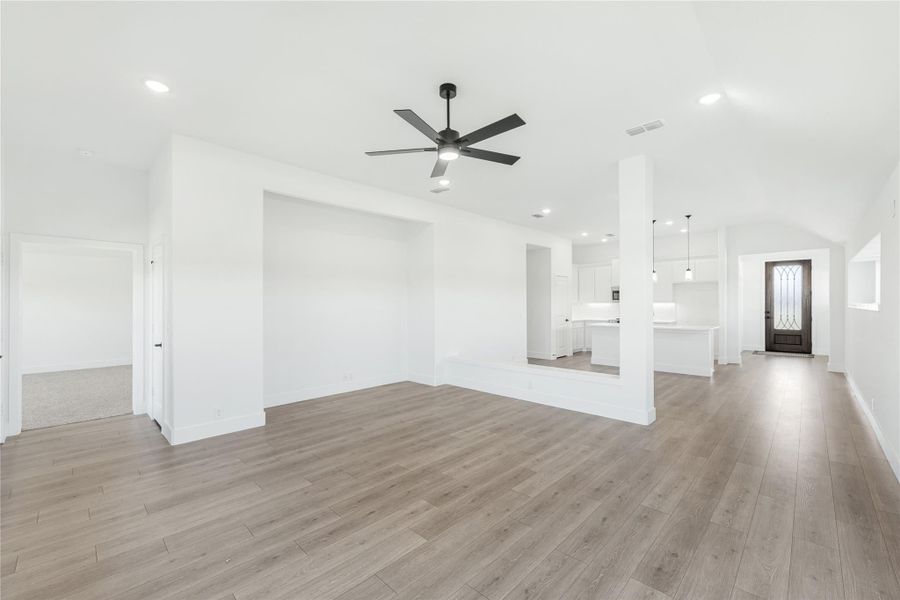 Open living area with wood-look floors, ceiling fan, and open view to kitchen and entry door