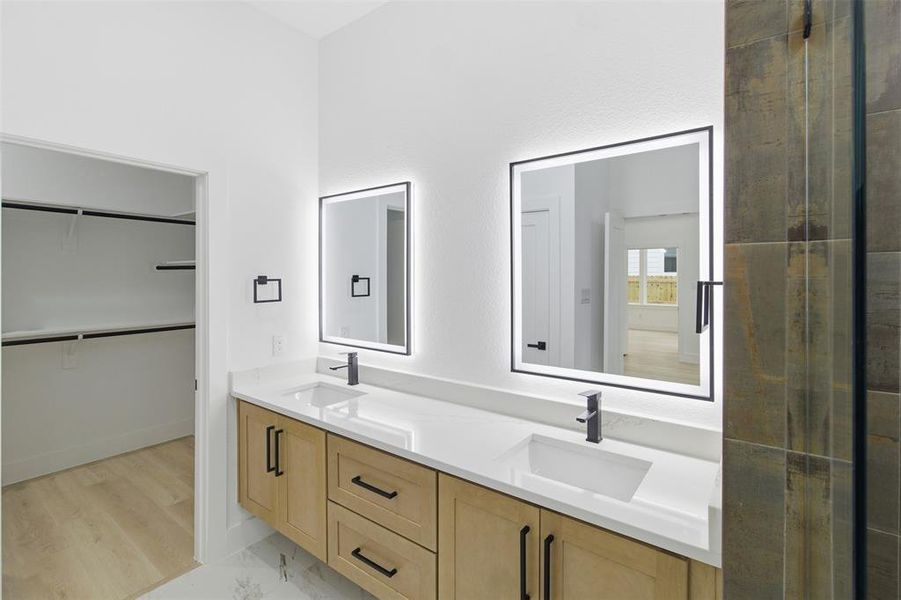 Bathroom featuring double vanity, a spacious closet, and light marble finish floors