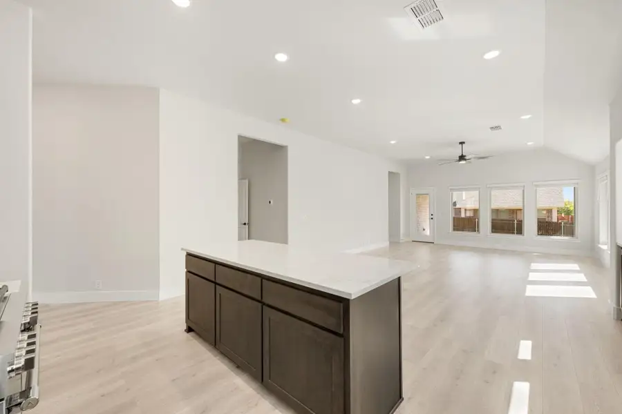 Open kitchen and living area with dark wood island, white countertop, light wood floors, and vaulted ceiling