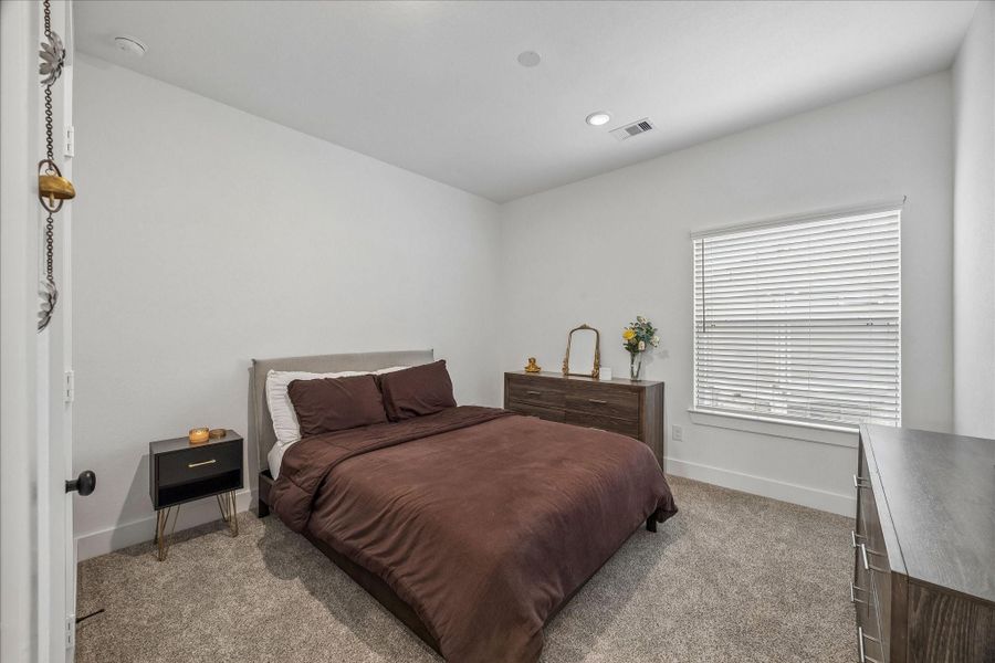 The secondary bedroom features oversized windows, high ceilings, recessed lighting, plush carpeting, and ample closet space, creating a bright and comfortable living space.
