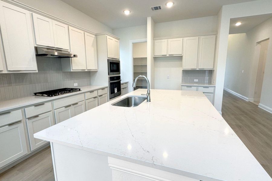 A well-appointed kitchen showcasing a spacious island with sink and modern built-in appliances.