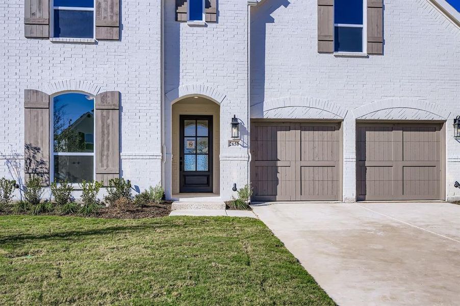 Doorway to property with concrete driveway, brick siding, a lawn, and a garage Doorway to property with concrete driveway, brick siding, a lawn, and a garage
