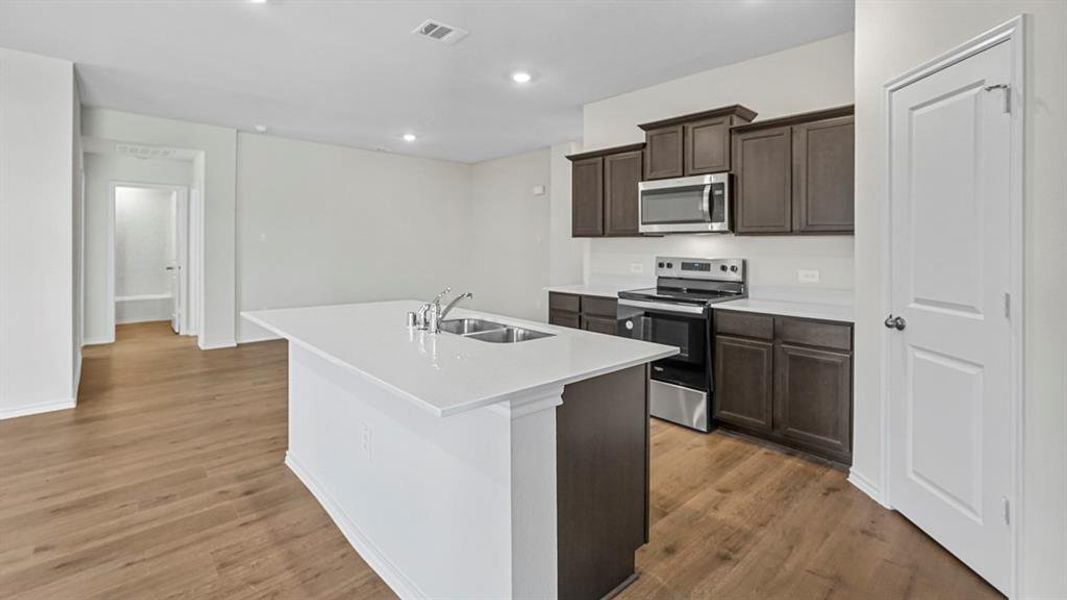 Kitchen featuring stainless steel appliances, dark wood finish cabinetry, a kitchen island with sink, light wood finished floors, and recessed lighting