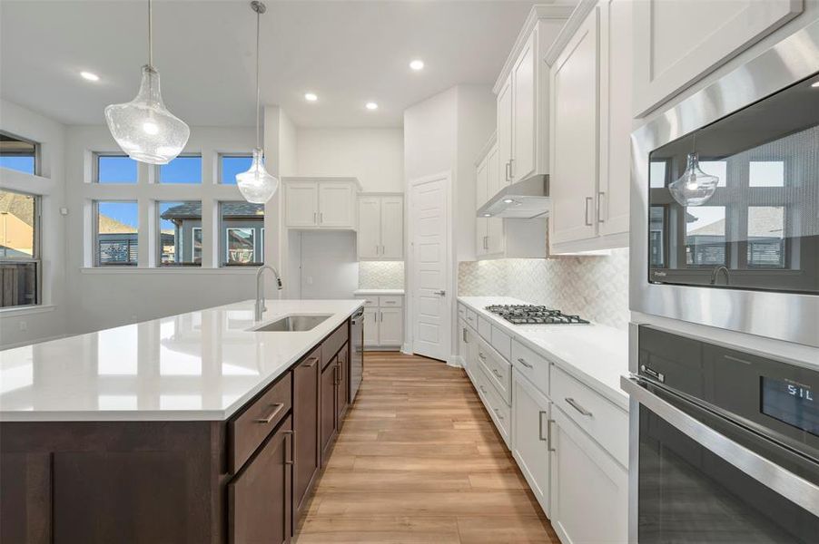 Kitchen with decorative backsplash, stainless steel appliances, dual tone cabinets, hanging light fixtures, and light wood-type flooring