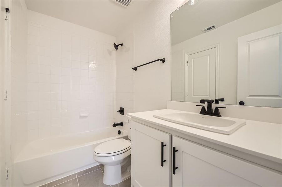 Full bathroom featuring vanity, tiled shower / bath combo, toilet, and tile patterned flooring