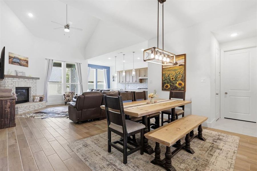 Open-concept living space featuring wood-finish flooring, a white brick fireplace with a mantle, and vaulted ceilings with a ceiling fan