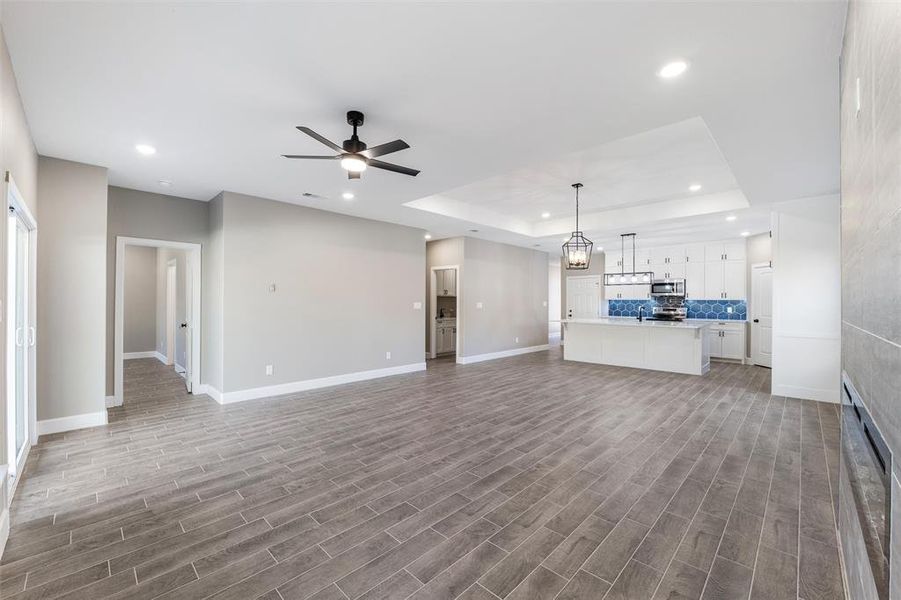 Unfurnished living room with hardwood / wood-style floors, a tray ceiling, and ceiling fan