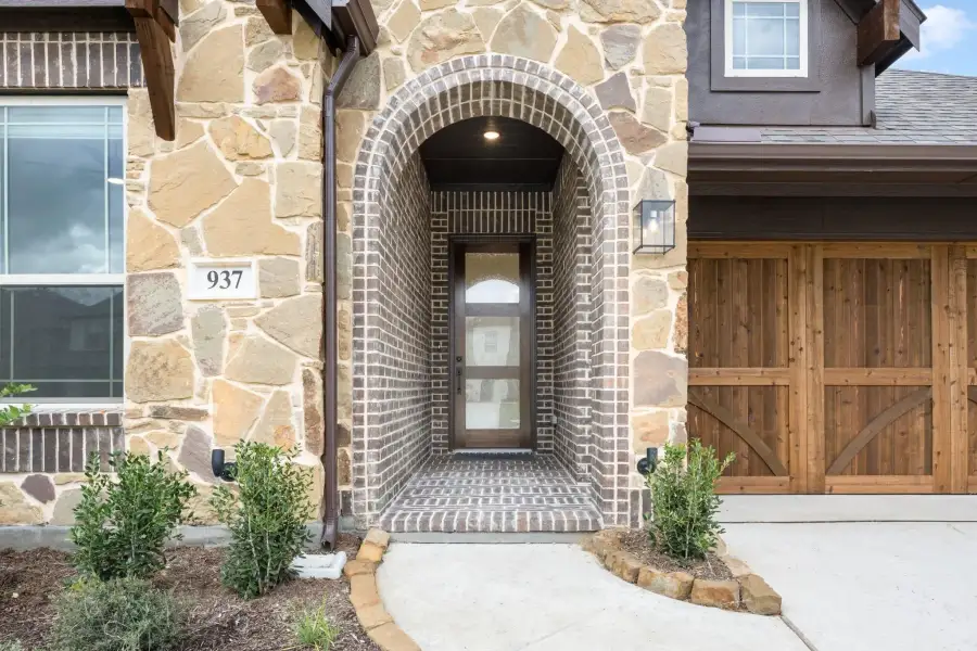 Home entrance with arched brick entryway, stone exterior, dark wood door, and wood garage door beside it