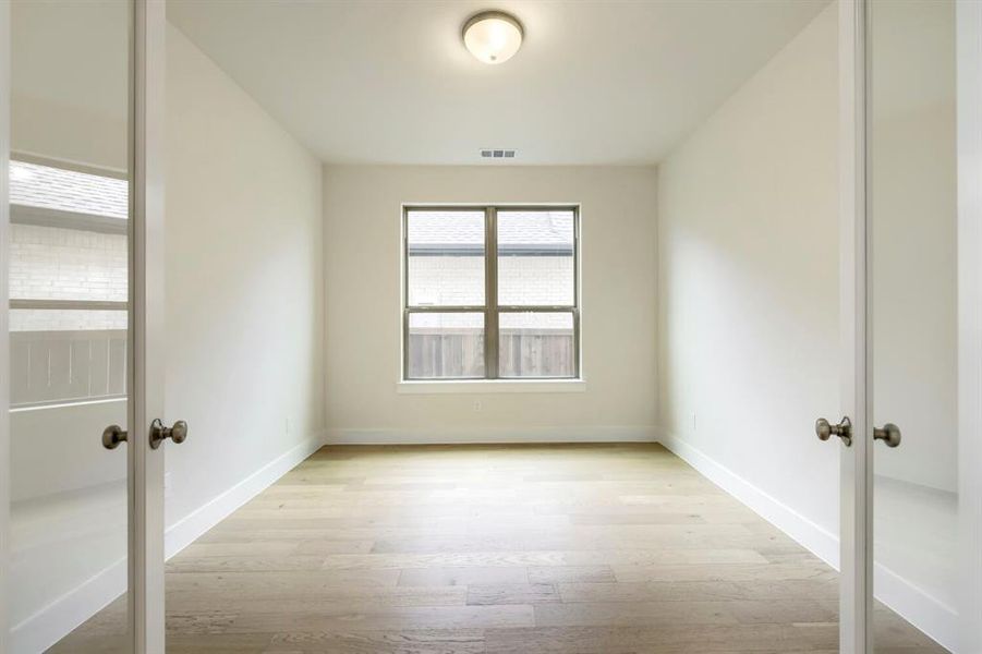 Room featuring wood-finish flooring, white baseboards, and neutral wall paint Room featuring wood-finish flooring, white baseboards, and neutral wall paint