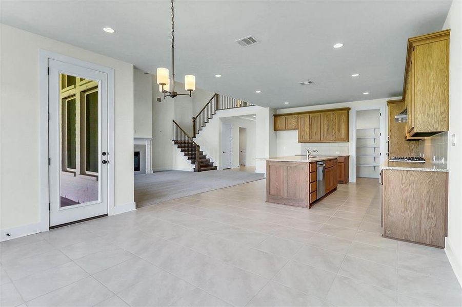 Kitchen and living area featuring tile flooring, wood-finish cabinetry, a central island with sink, a gas cooktop, and a fireplace with mantle Kitchen and living area featuring tile flooring, wood-finish cabinetry, a central island with sink, a gas cooktop, and a fireplace with mantle