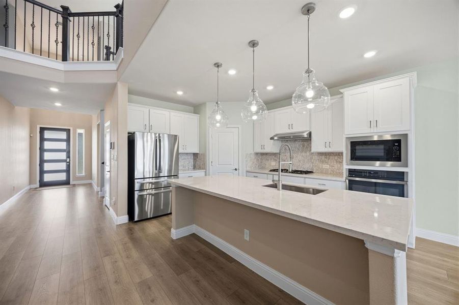 Kitchen with stainless steel appliances, light stone countertops, white cabinets, light wood-style flooring, and decorative backsplash.