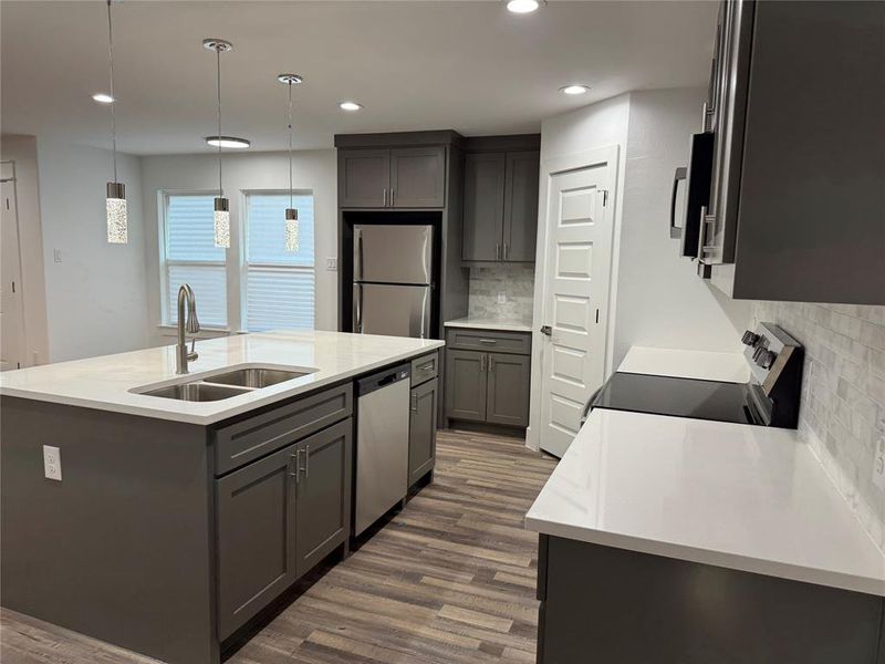 Kitchen featuring dark hardwood / wood-style flooring, sink, hanging light fixtures, appliances with stainless steel finishes, and a center island with sink