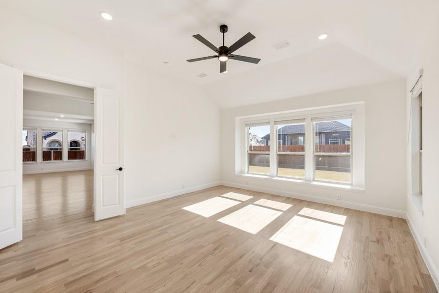 Empty bedroom with light wood floors, ceiling fan, and large windows with neighborhood view
