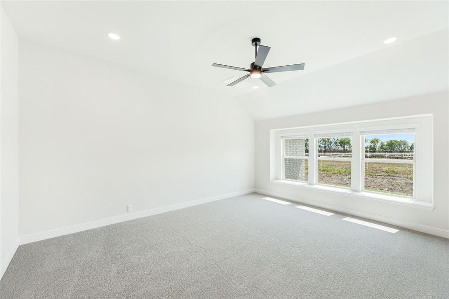 Empty bedroom with vaulted ceiling, ceiling fan, gray carpet, and large windows overlooking a yard
