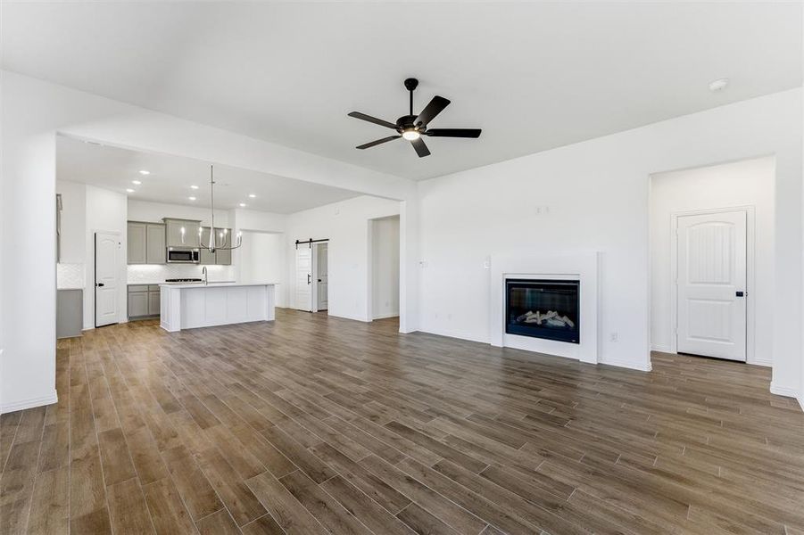 Unfurnished living room featuring ceiling fan, a barn door, dark wood finished floors, a glass covered fireplace, and recessed lighting