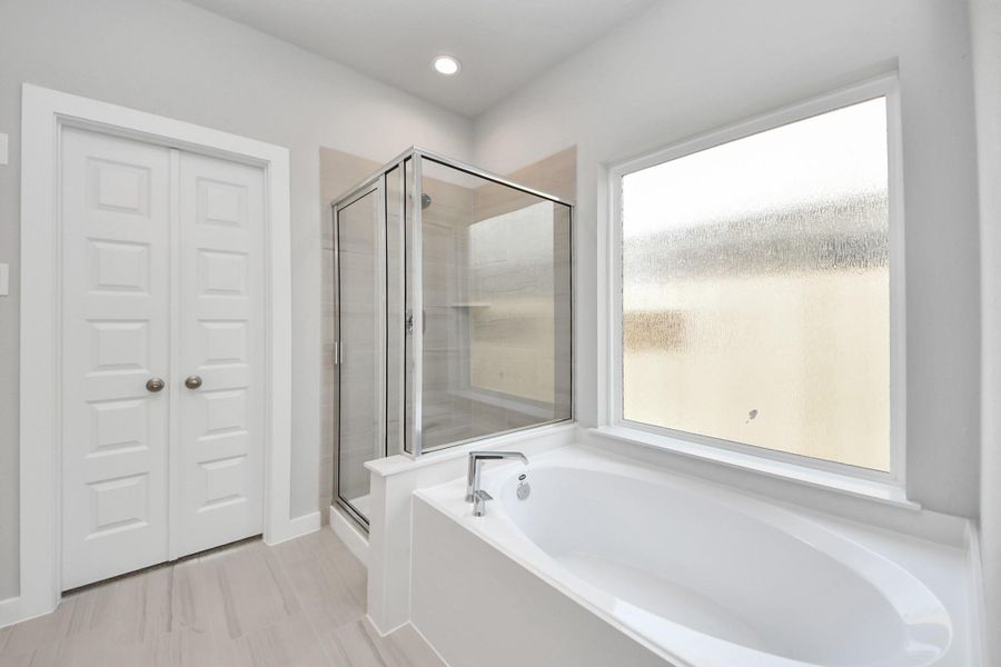 Escape to a spa-like oasis in this primary bathroom. Enjoy a walk-in shower with tile surround, a separate garden tub with custom detailing, and an elegant vanity featuring light countertops, modern hardware, and beautiful recessed lights. Experience luxury and relaxation in every detail! Sample photo of completed home with similar floor plan. Actual colors and selections may vary. Escape to a spa-like oasis in this primary bathroom. Enjoy a walk-in shower with tile surround, a separate garden tub with custom detailing, and an elegant vanity featuring light countertops, modern hardware, and beautiful recessed lights. Experience luxury and relaxation in every detail! Sample photo of completed home with similar floor plan. Actual colors and selections may vary.
