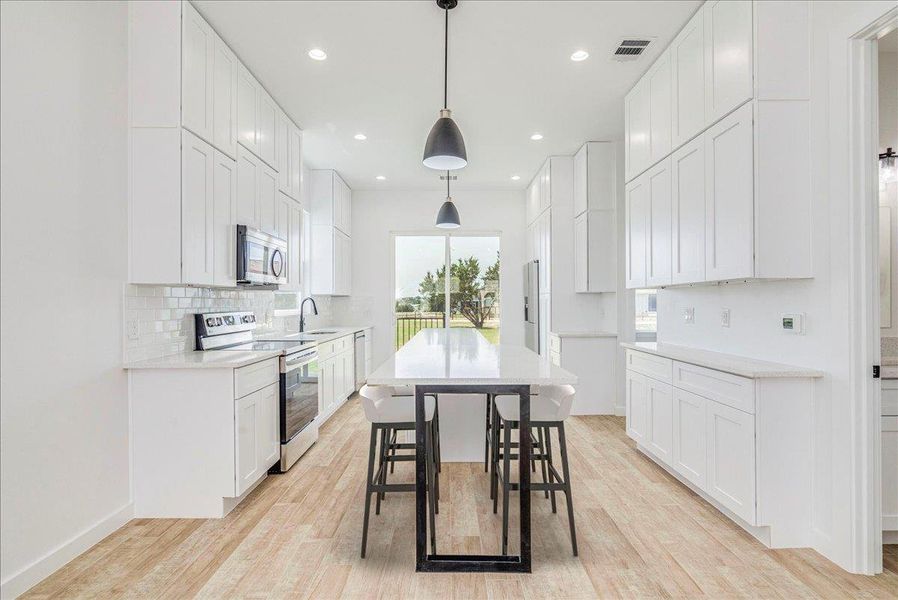 Open kitchen with eat in quartz countertop and stainless steel appliances.