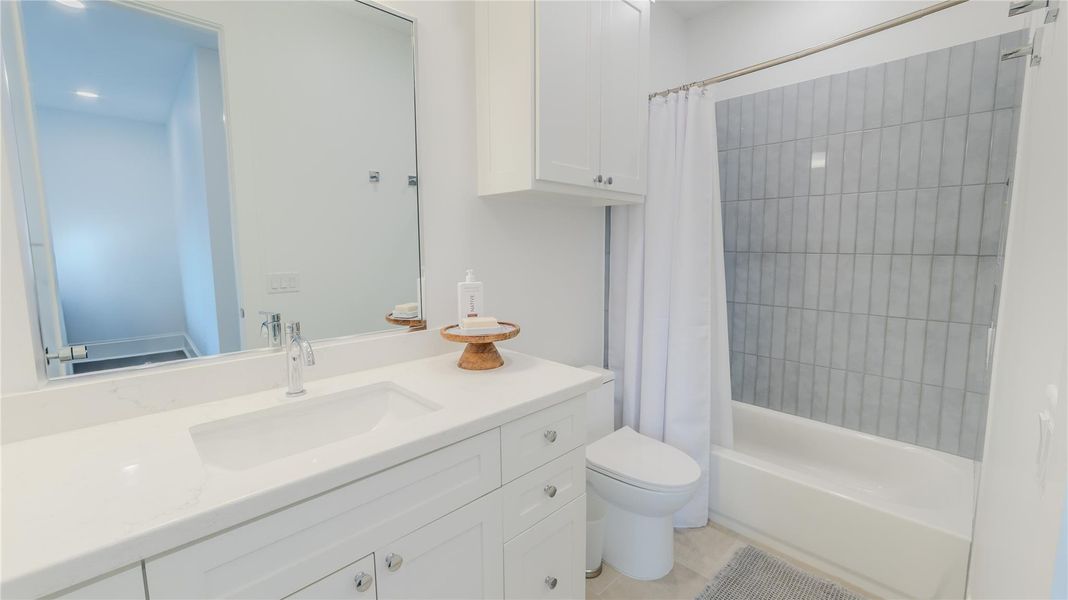 This bathroom features a sleek, modern design with a large mirror, white cabinetry, and a clean countertop. It includes a bathtub with a tiled shower area and a simple white shower curtain, creating a bright and inviting space.