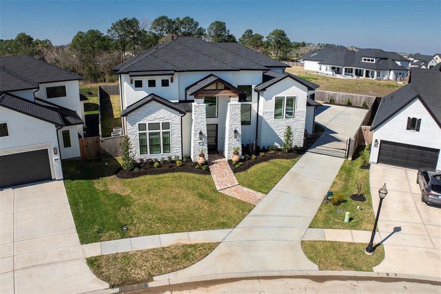 This photo showcases a modern two-story home with a sleek black roof and a light exterior. The property features a neat, landscaped front yard with a paved driveway leading to a spacious garage. It's set in a suburban neighborhood with nearby houses and a backdrop of trees.