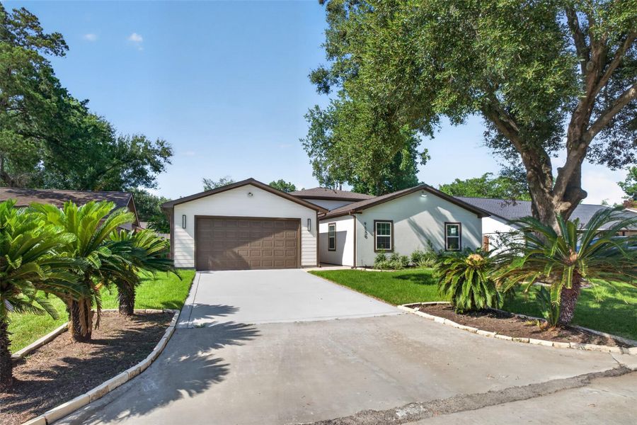 Charming single-story home with a spacious driveway, attached garage, and lush landscaping featuring mature trees and well-maintained greenery.
