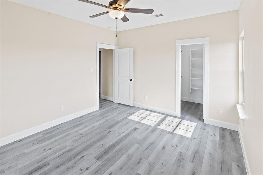 Unfurnished bedroom featuring ceiling fan, a walk in closet, a closet, and light wood-type flooring